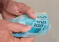 Mãos segurando cédulas de R$ 100 em referência à nova previsão do salário mínimo de 2027.