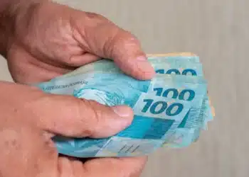 Mãos segurando cédulas de R$ 100 em referência à nova previsão do salário mínimo de 2027.