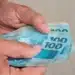 Mãos segurando cédulas de R$ 100 em referência à nova previsão do salário mínimo de 2027.