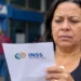 Segurada analisa documento do INSS diante de uma agência bancária, representando a proposta de pagamento em dobro em casos de benefício negado injustamente.