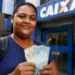 Mulher segura notas de dinheiro em frente a uma agência bancária, representando o pagamento do 4º lote da restituição do IRPF 2026.