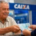 Idoso recebe dinheiro em agência bancária representando os pagamentos do INSS de agosto para beneficiários que recebem até um salário mínimo.