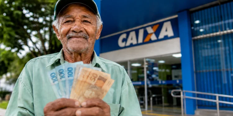Idoso segura cédulas em frente a uma agência da Caixa, representando os pagamentos do INSS e do BPC em agosto.