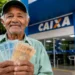 Idoso segura cédulas em frente a uma agência da Caixa, representando os pagamentos do INSS e do BPC em agosto.