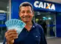 Pessoa segurando cédulas de real em frente a uma agência bancária, representando os pagamentos do INSS de até R$ 8.475,55 em agosto de 2026.