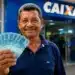 Pessoa segurando cédulas de real em frente a uma agência bancária, representando os pagamentos do INSS de até R$ 8.475,55 em agosto de 2026.