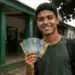 Estudante da EJA segura cédulas de real em frente a uma escola pública, representando o programa Pé-de-Meia.