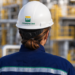 Profissional uniformizada da Transpetro vista de costas em área industrial, com capacete de segurança identificado com a marca da empresa.