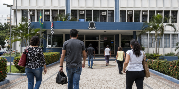 Pessoas caminham em direção a uma prefeitura, em referência aos processos seletivos com vagas de nível médio em Minas Gerais.