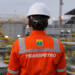 Trabalhador da Transpetro com uniforme de segurança em área industrial de petróleo e gás.