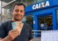 Homem segurando notas de real em frente a uma agência da Caixa, representando o pagamento do quarto lote da restituição do IRPF 2026.