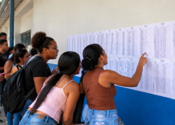 Candidatos consultam lista de convocação publicada em parede de instituição de ensino.