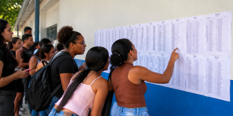 Candidatos consultam lista de convocação publicada em parede de instituição de ensino.