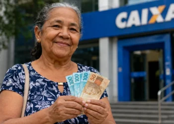 Idosa segura cédulas em frente a uma agência da Caixa, em referência ao reajuste do salário mínimo e aos benefícios do INSS e BPC em 2027.