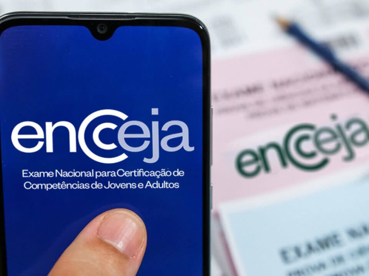 Imagem ilustrativa de celular com a marca do Encceja na tela diante de cartões-resposta do exame, em referência à regra que separa a reaplicação por turno