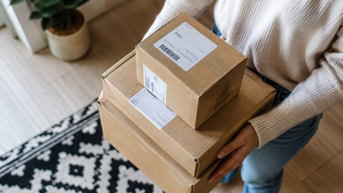 Pessoa segura caixas de compras online, representando a possível volta do imposto de 20% sobre encomendas internacionais.