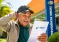 Idoso segura documento do INSS em frente à agência da Previdência Social, representando a aposentadoria por idade.