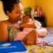 Mãe segura recém-nascido em casa, com documento da Previdência Social sobre a mesa, representando o salário-maternidade do INSS.