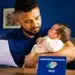 Pai segura bebê recém-nascido enquanto consulta documento relacionado ao INSS sobre salário-maternidade.