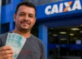 Trabalhador segura cédulas em frente a uma agência da Caixa, representando o fim do período de saque-aniversário do FGTS para os nascidos em junho.