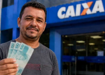 Trabalhador segura cédulas em frente a uma agência da Caixa, representando o fim do período de saque-aniversário do FGTS para os nascidos em junho.