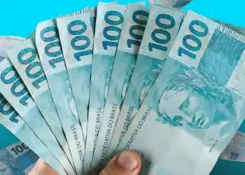 Notas de R$ 100 sendo seguradas, representando o Saque Calamidade de R$ 6.220 para moradores de 20 cidades.