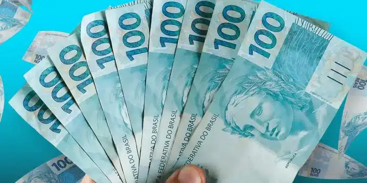 Notas de R$ 100 sendo seguradas, representando o Saque Calamidade de R$ 6.220 para moradores de 20 cidades.