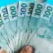Notas de R$ 100 sendo seguradas, representando o Saque Calamidade de R$ 6.220 para moradores de 20 cidades.