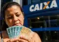 Mulher em frente a uma agência da Caixa segurando cédulas de real, representando o Saque Calamidade do FGTS liberado para moradores do Rio Grande do Sul.