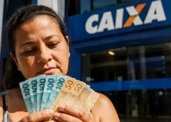 Mulher em frente a uma agência da Caixa segurando cédulas de real, representando o Saque Calamidade do FGTS liberado para moradores do Rio Grande do Sul.