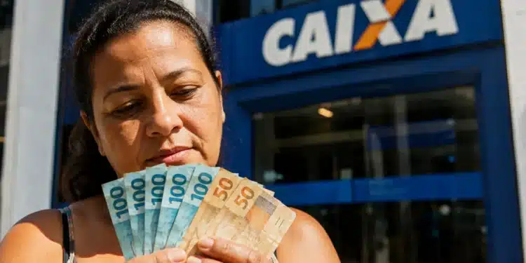 Mulher em frente a uma agência da Caixa segurando cédulas de real, representando o Saque Calamidade do FGTS liberado para moradores do Rio Grande do Sul.