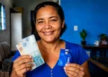 Mulher segura dinheiro e cartão da CAIXA, ilustrando a liberação do Saque Calamidade de até R$ 6.220.