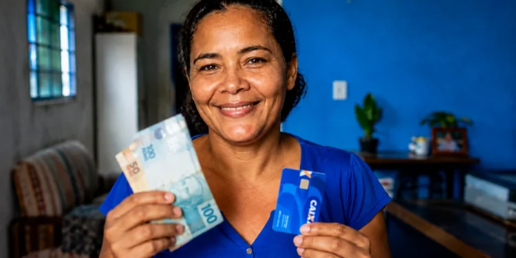 Mulher segura dinheiro e cartão da CAIXA, ilustrando a liberação do Saque Calamidade de até R$ 6.220.
