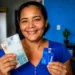 Mulher segura dinheiro e cartão da CAIXA, ilustrando a liberação do Saque Calamidade de até R$ 6.220.