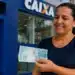 Mulher segura cédulas em frente a uma agência da Caixa, representando a solicitação do saque de R$ 6.220 do FGTS.