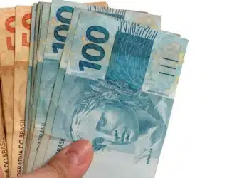 Mão segurando cédulas de reais representando o saque do FGTS de R$ 6.220
