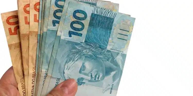 Mão segurando cédulas de reais representando o saque do FGTS de R$ 6.220