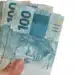 Mão segurando cédulas de reais representando o saque do FGTS de R$ 6.220