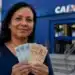 Mulher segura cédulas em frente a uma agência da Caixa, representando a liberação do saque do FGTS de até R$ 6,2 mil para moradores de 19 cidades.