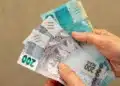 Mãos segurando notas de real representando o saque do FGTS autorizado pela Caixa para moradores de SP, MG e RS