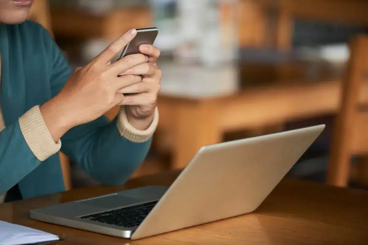 Pessoa utiliza celular ao lado de notebook para acessar serviços digitais pela internet.