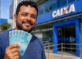 Trabalhador segura cédulas diante de uma agência da Caixa, ilustrando o saque de até R$ 6,2 mil do FGTS.