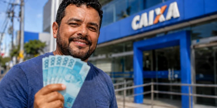 Trabalhador segura cédulas diante de uma agência da Caixa, ilustrando o saque de até R$ 6,2 mil do FGTS.