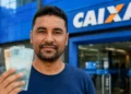 Homem segura dinheiro em frente a uma agência da Caixa representando o saque de R$ 6.220 do FGTS.