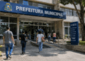 Pessoas entrando em prédio de prefeitura municipal, representando concursos públicos e processos seletivos com vagas abertas.