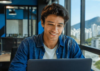 Jovem profissional utilizando notebook em escritório moderno, representando oportunidades de estágio, jovem aprendiz e trainee no Rio de Janeiro.