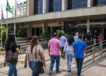 Pessoas caminham em direção a prédio público, representando oportunidades de processos seletivos para nível médio.