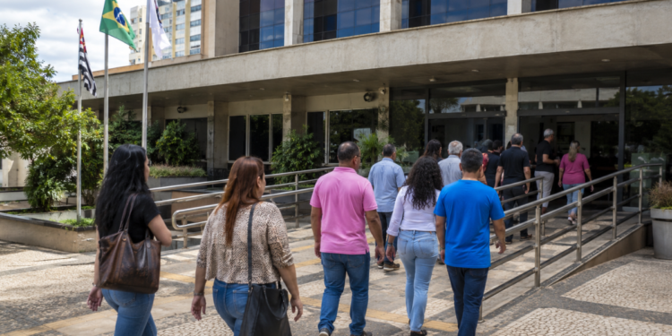 Pessoas caminham em direção a prédio público, representando oportunidades de processos seletivos para nível médio.