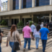 Pessoas caminham em direção a prédio público, representando oportunidades de processos seletivos para nível médio.