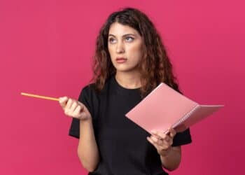 Imagem ilustrativa de mulher com expressão pensativa segurando um caderno e um lápis, representando a dúvida na hora de escrever a palavra